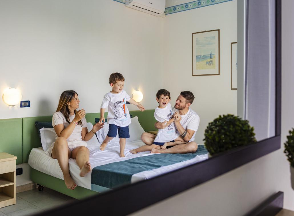 Famille joyeuse joue sur le lit, rires et bonheur emplissent la pièce.