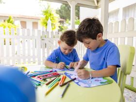 Due bambini disegnano felici all'aperto, circondati da colori vivaci.