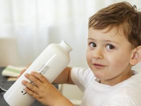 Happy child holds a white bottle, sitting at a table.