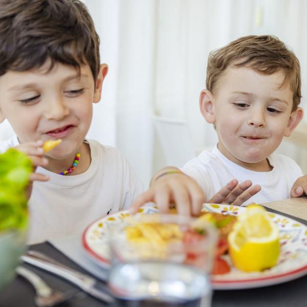 Two smiling kids share a colorful, delicious meal.