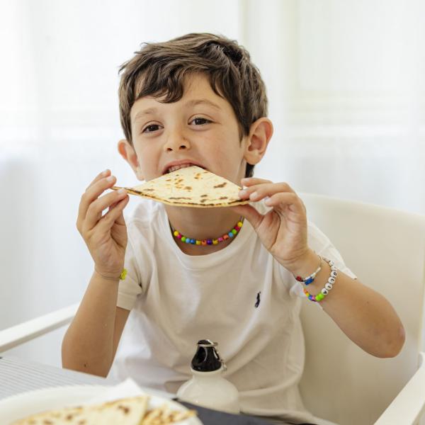 Happy child eagerly eats a flatbread with joy.